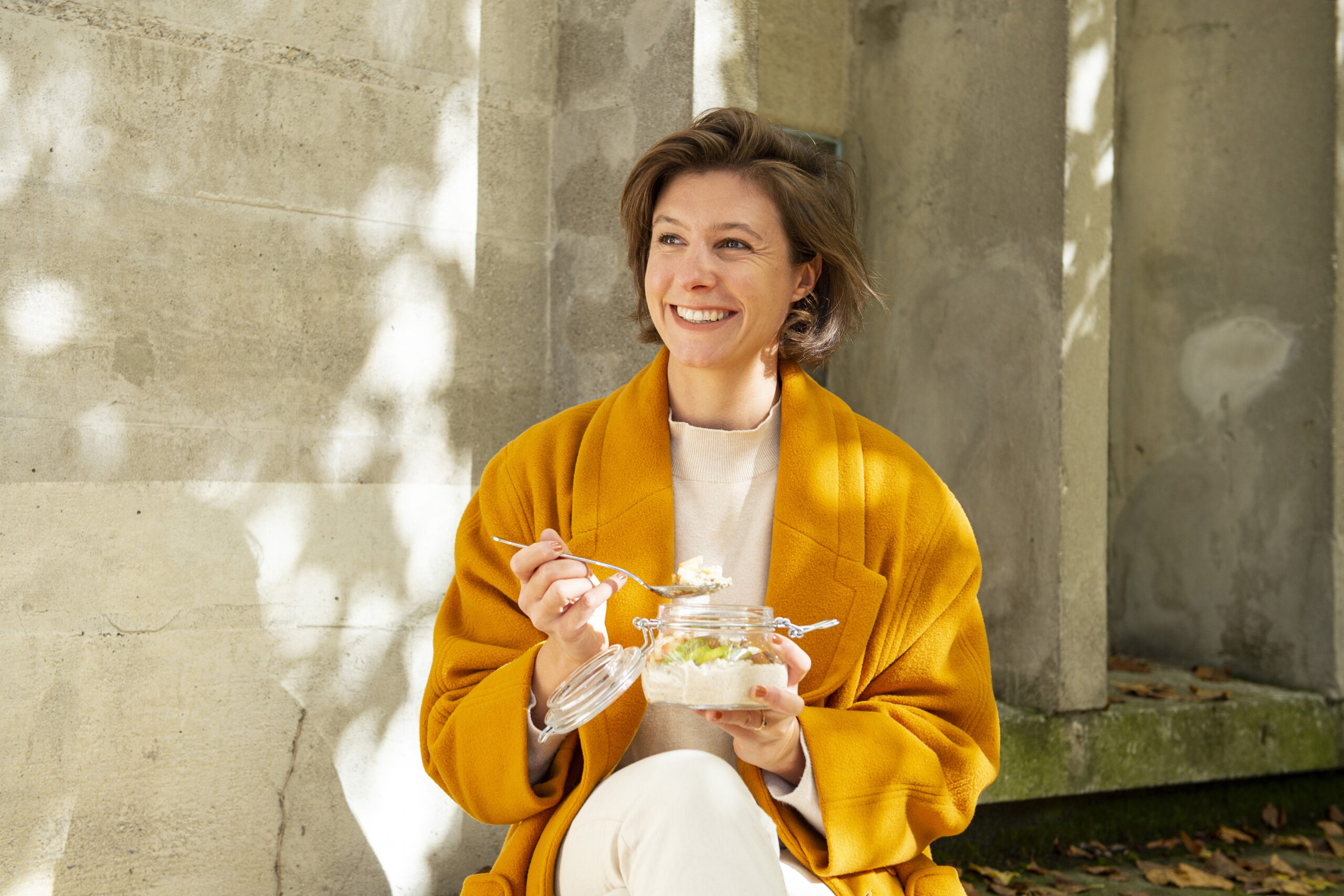 Porridge selber machen: Person im gelben Mantel isst aus Glasbehälter. Szene inspiriert zum Selbermachen.